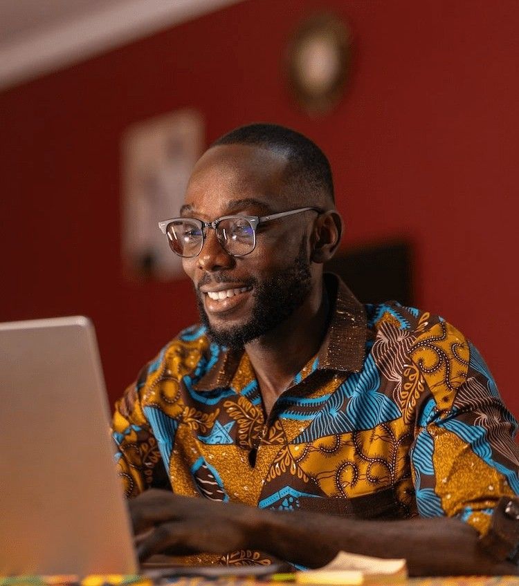 A happy man, wearing glasses and a vibrant shirt, studying programming on his laptop.