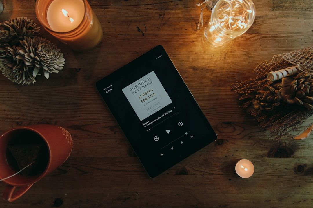 A tablet displaying an audiobook on a wooden table surrounded by lit candles, a mug of tea, and decorative autumn elements.