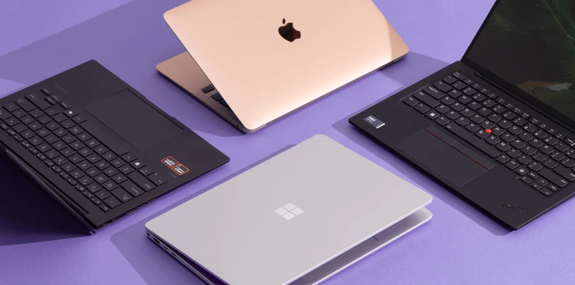 Multiple laptops from different brands displayed on a table, including Apple, Microsoft, and Lenovo devices for comparing computer options.