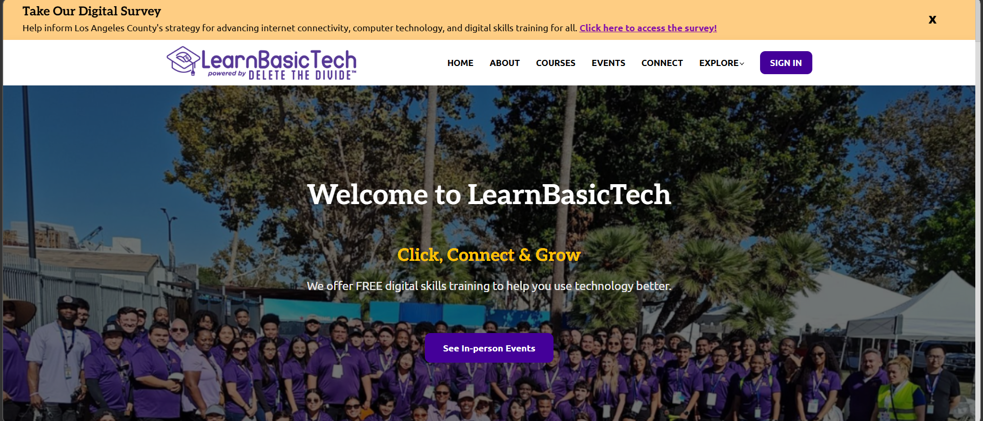 Homepage banner for the LearnBasicTech website showing the site navigation menu, logo, a survey announcement at the top, and a large group of people standing outdoors in front of trees and event tents.
