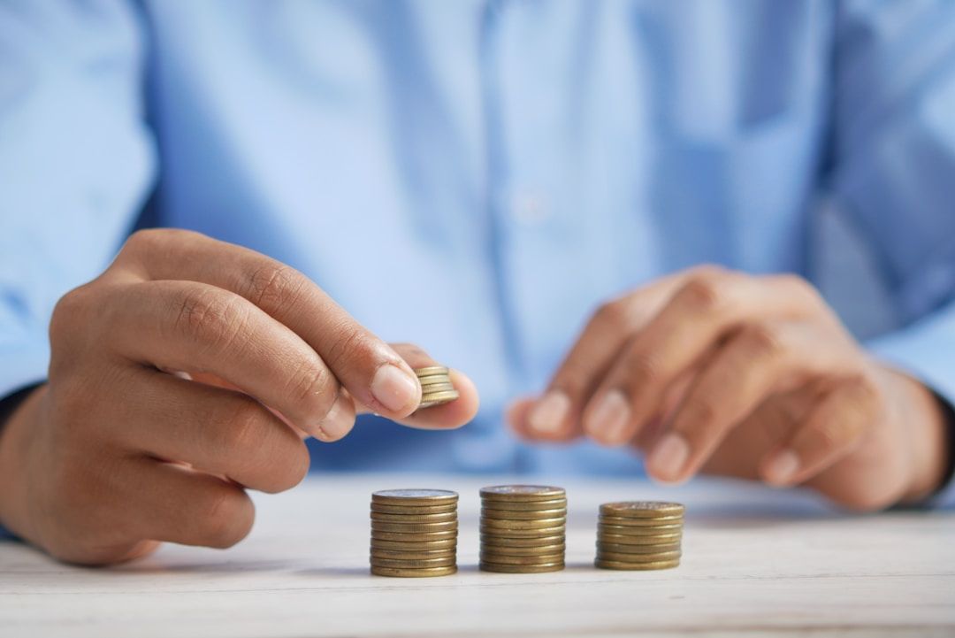 Close-up of hands stacking several small piles of coins on a light-colored surface.
