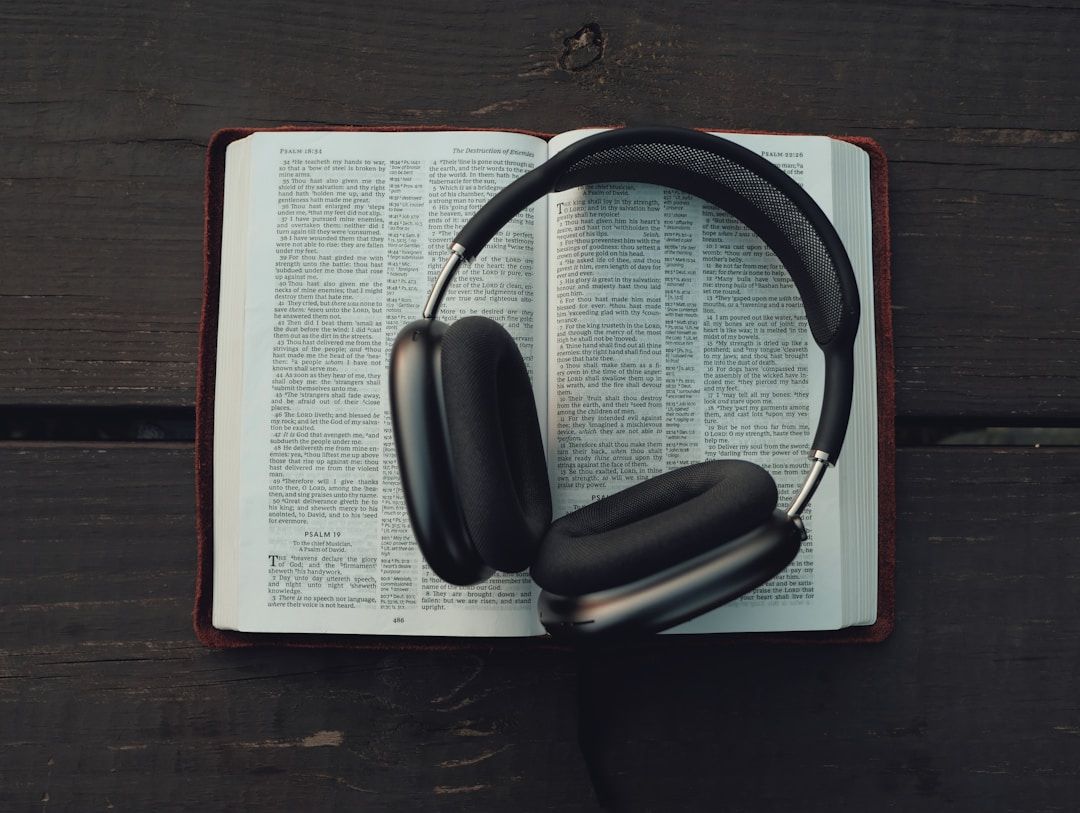A pair of over-ear headphones resting on an open book laid on a dark wooden surface.