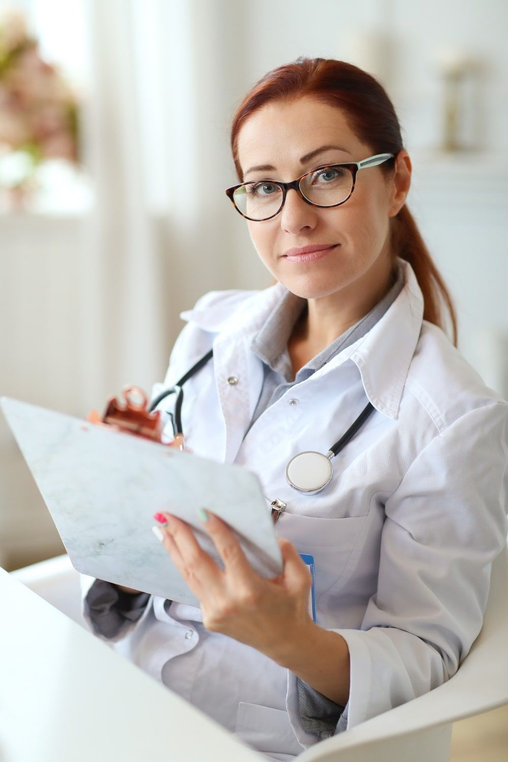 A female doctor is reading blood test results from a clipboard she is holding.
