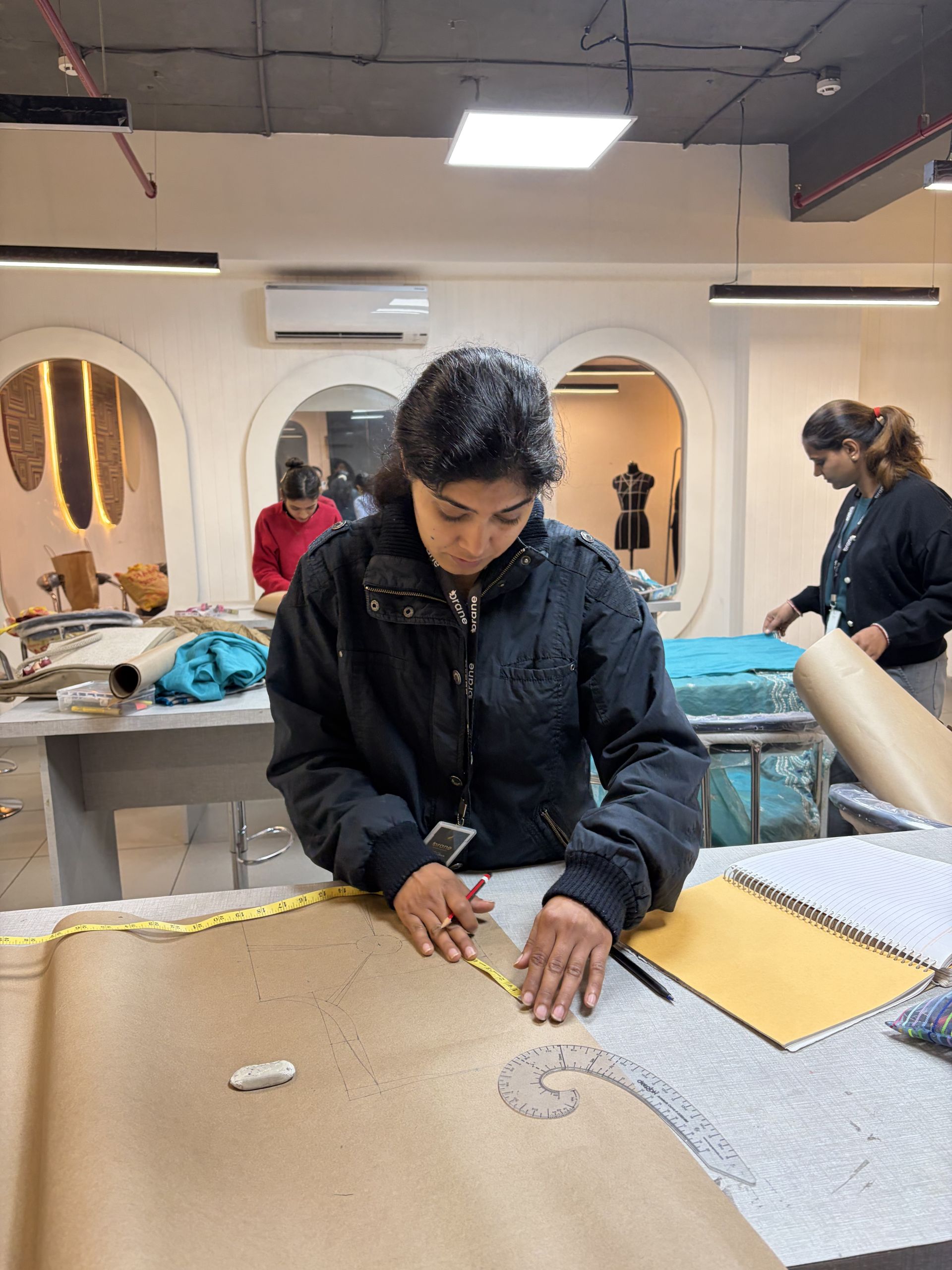 Orane student drafting a garment pattern on paper with a measuring tape and French curve
