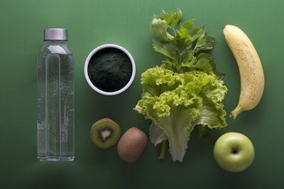 Healthy food arrangement with green vegetables, banana, apple, and a water bottle on a green background