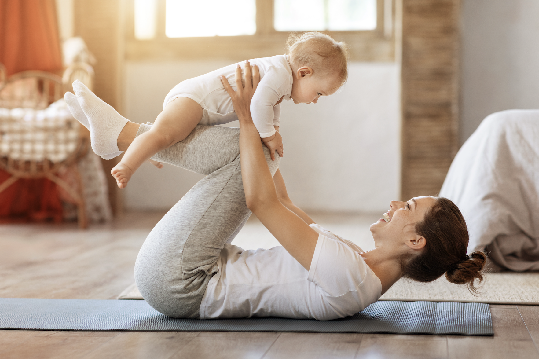 junge Mama h&auml;lt Baby &uuml;ber sich und liegt auf der Yogamatte