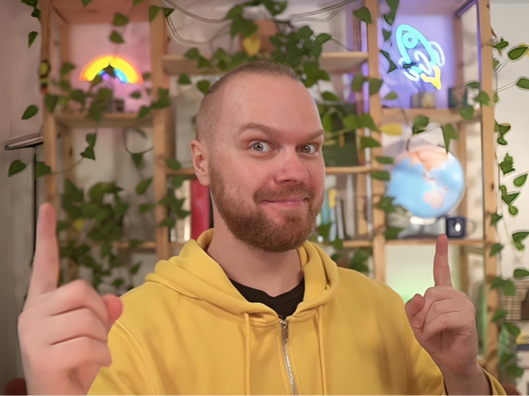 Norbert in his studio, pointing upward, with neon rainbow and rocket-shaped lamps in the background.