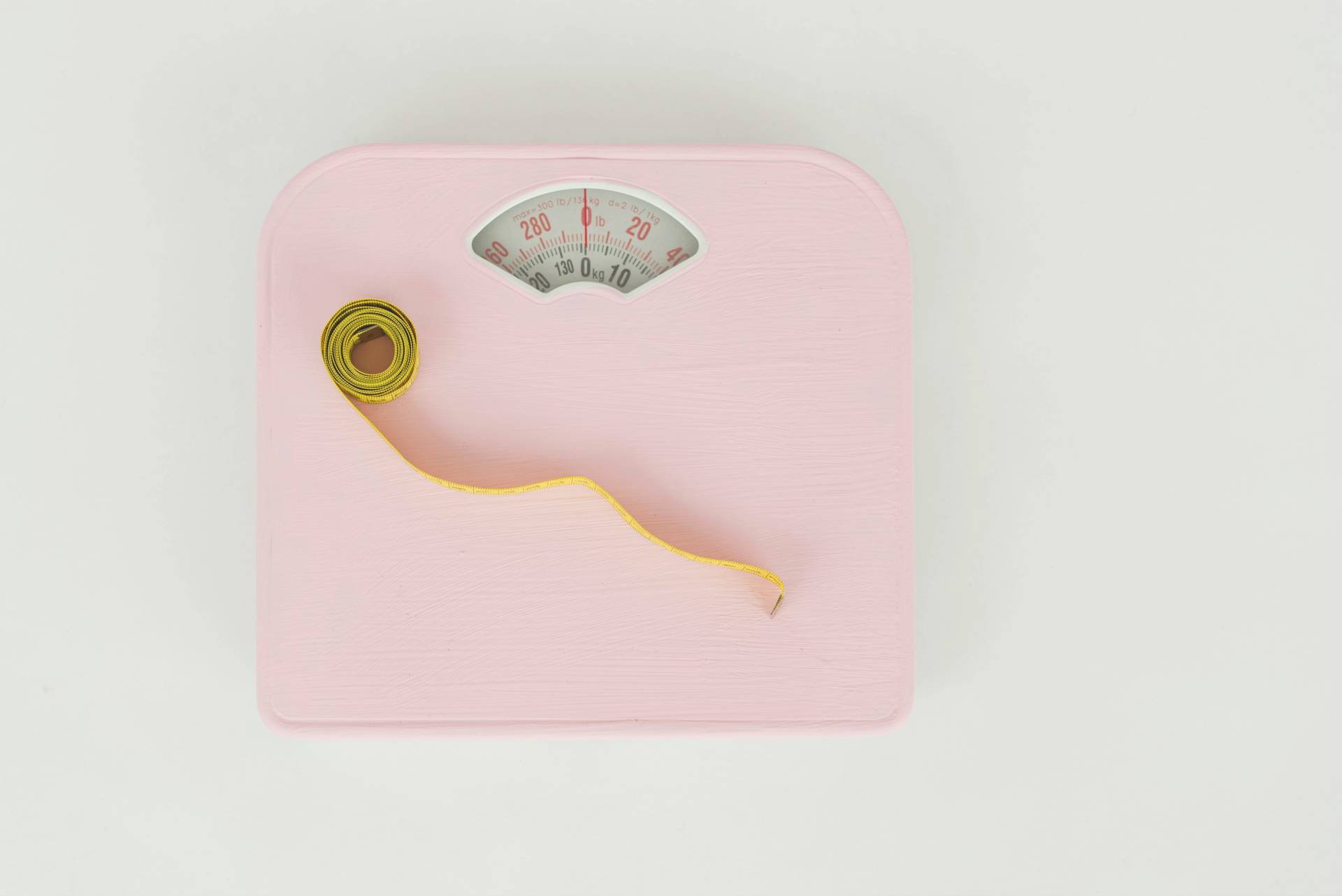 Pink vægt med gult målband, der symboliserer beregning af BMI (Body Mass Index) og måling af vægt som en del af sundhedsstrategier