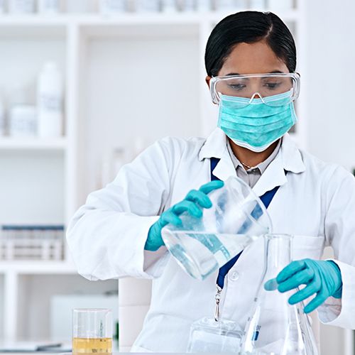 Lab Worker in full protective equipment pouring clear liquid between flasks