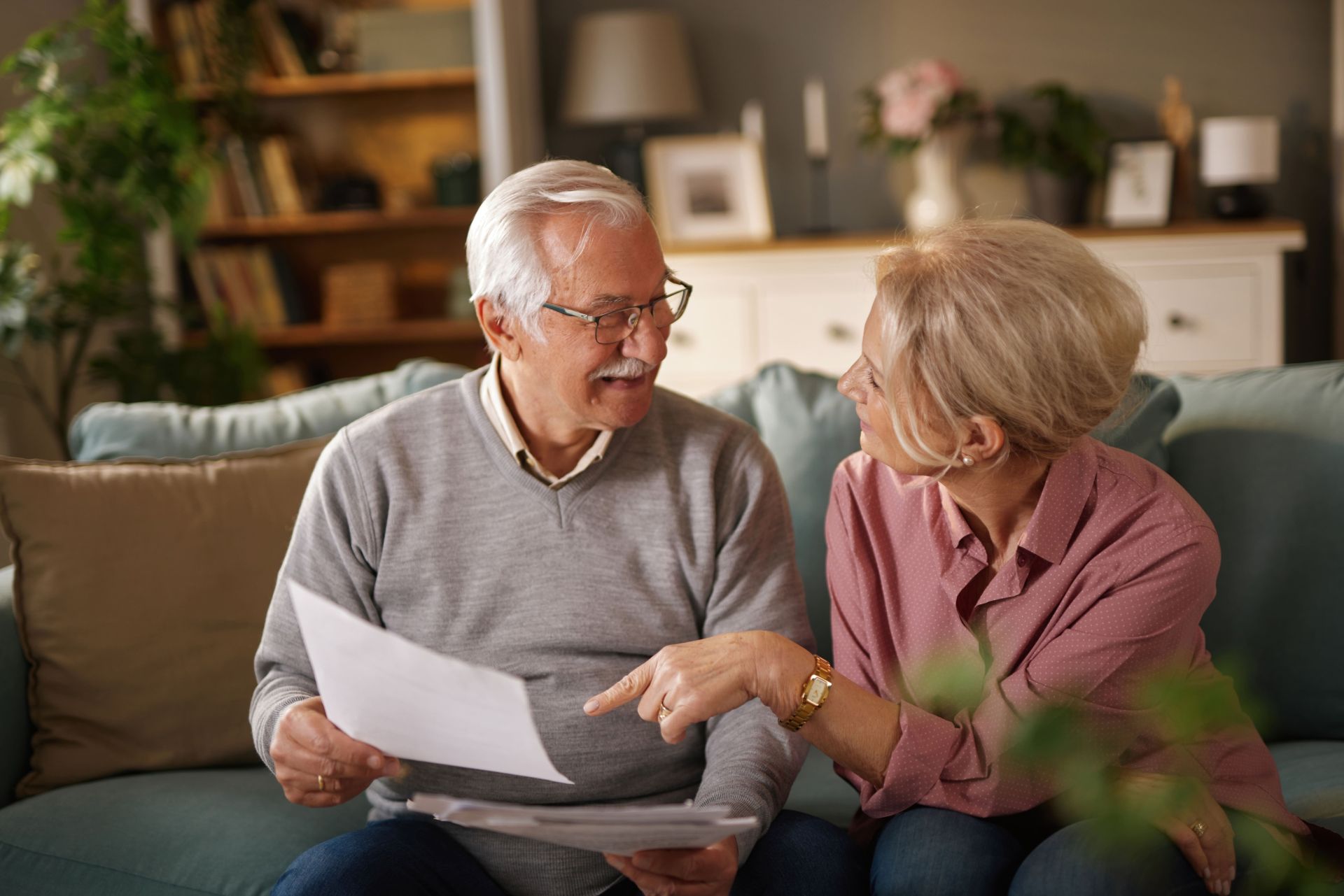 Ein älteres Paar sitzt gemeinsam auf dem Sofa und bespricht Unterlagen – ein Moment, der zeigt, wie wichtig gute Organisation ist, um Pflege und Beruf vereinbaren zu können.