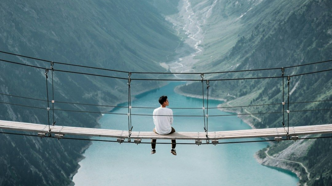 a man sat on a bridge overlooking a valley with water