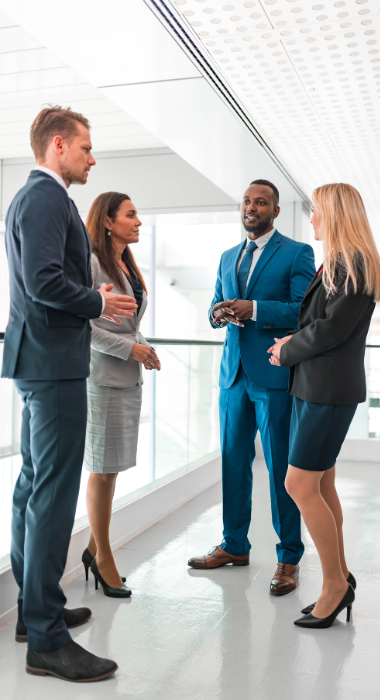 Two professional men and two professional women ,all wearing suits, talking while standing and facing each other