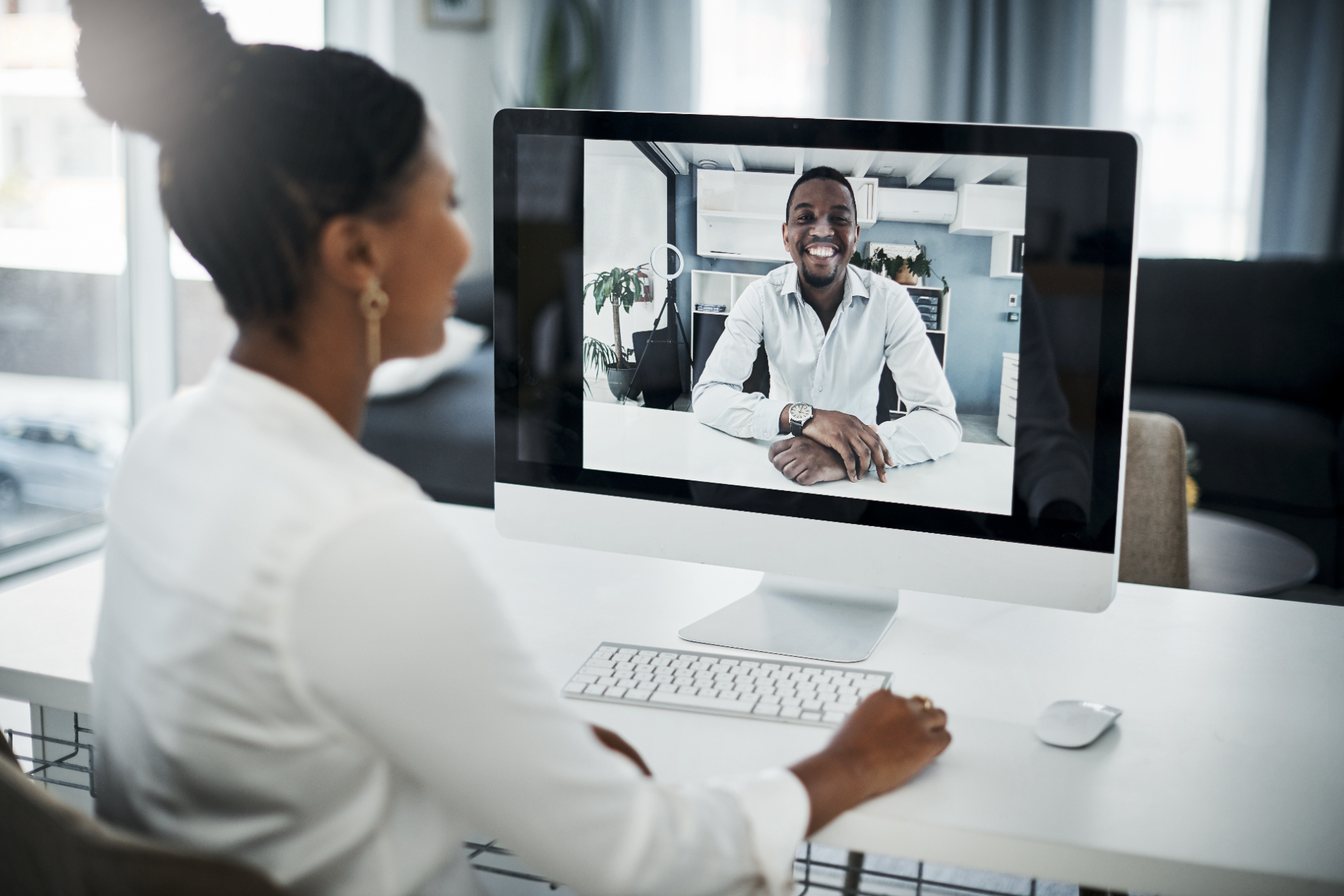 A woman and a man engaged in a video call, highlighting remote team collaboration for compliance training. The woman is sitting at a desk, interacting with the man displayed on her computer monitor.