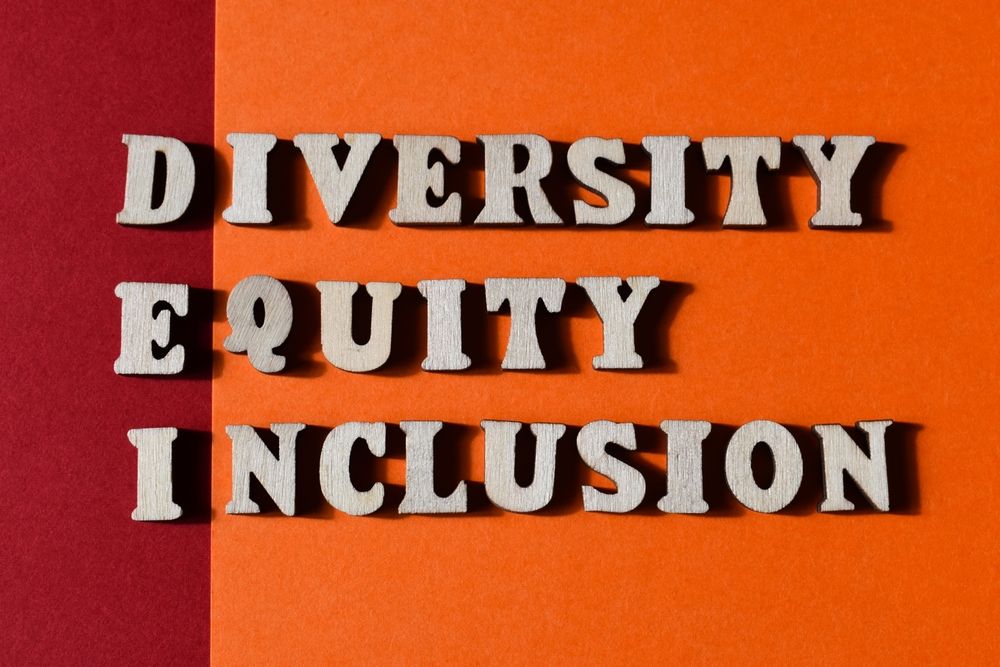 Wooden letters spelling out Diversity, Equity, and Inclusion on a split red and orange background. A vibrant visual representation promoting workplace diversity, equity, and inclusion principles. Ideal for DEI initiatives, advocacy programs, and corporate culture enhancement content.