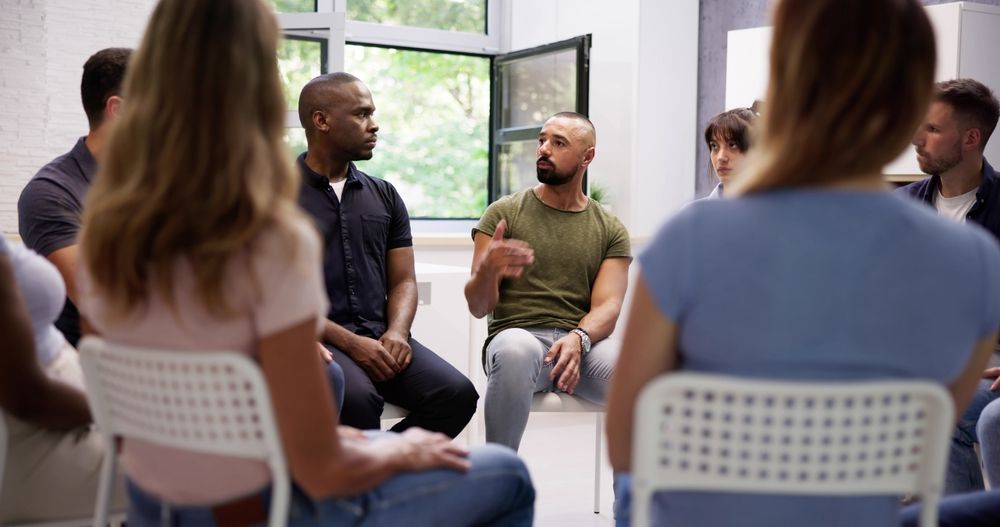 Group discussion in a bright, modern setting with diverse participants seated in a circle. This image illustrates collaboration, open communication, and teamwork, fostering a sense of inclusion and mutual understanding in a supportive environment.