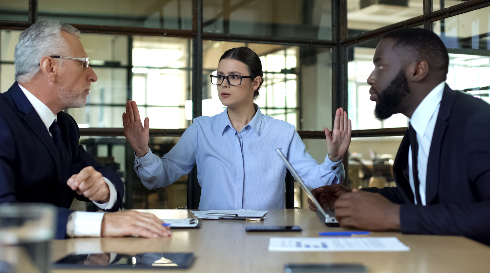 Office conflict resolution scene with a female mediator calmly intervening between two male colleagues in a heated discussion. This image illustrates the importance of conflict management, effective communication, and maintaining a collaborative workplace environment.