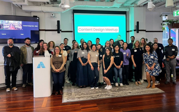 Event attendees at the Content Design Meetup, smiling in a huddle surrounding the host and guest speaker.