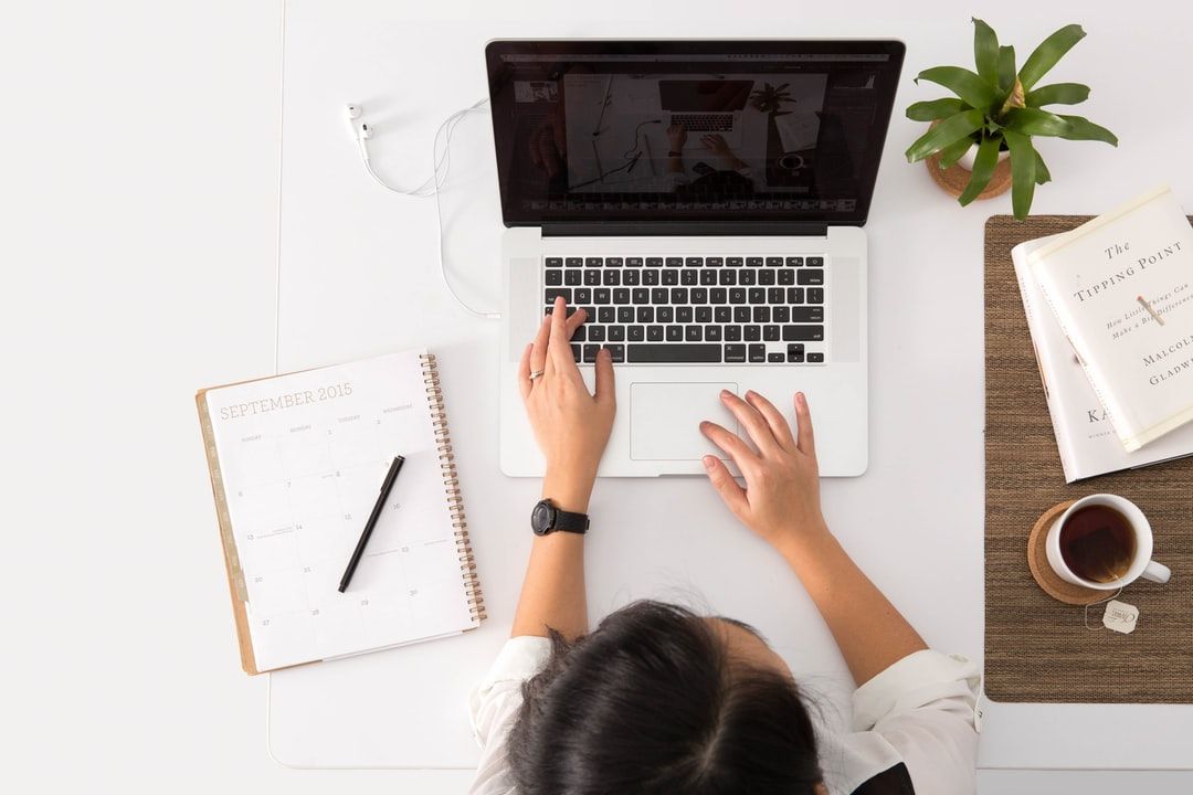 Overhead view of a person working on a laptop, surrounded by a calendar, notebook, potted plant, and coffee cup on a clean desk; an inspiring setup for productivity and organization.