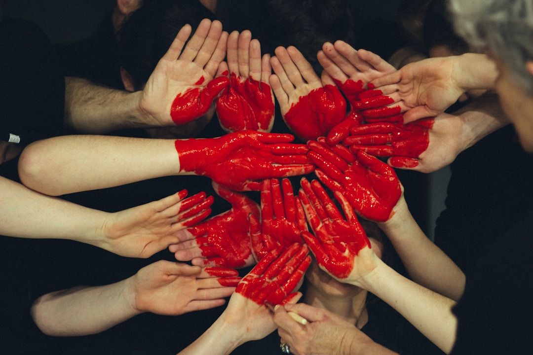 a group of hands with a red heart painted on them to symbolize empathy, the siddhi of gene key 13