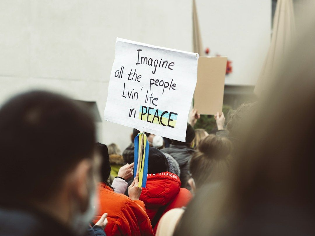 Protester holding a sign that says Imagine All the People Livin Life in Peace - Gene Key 4