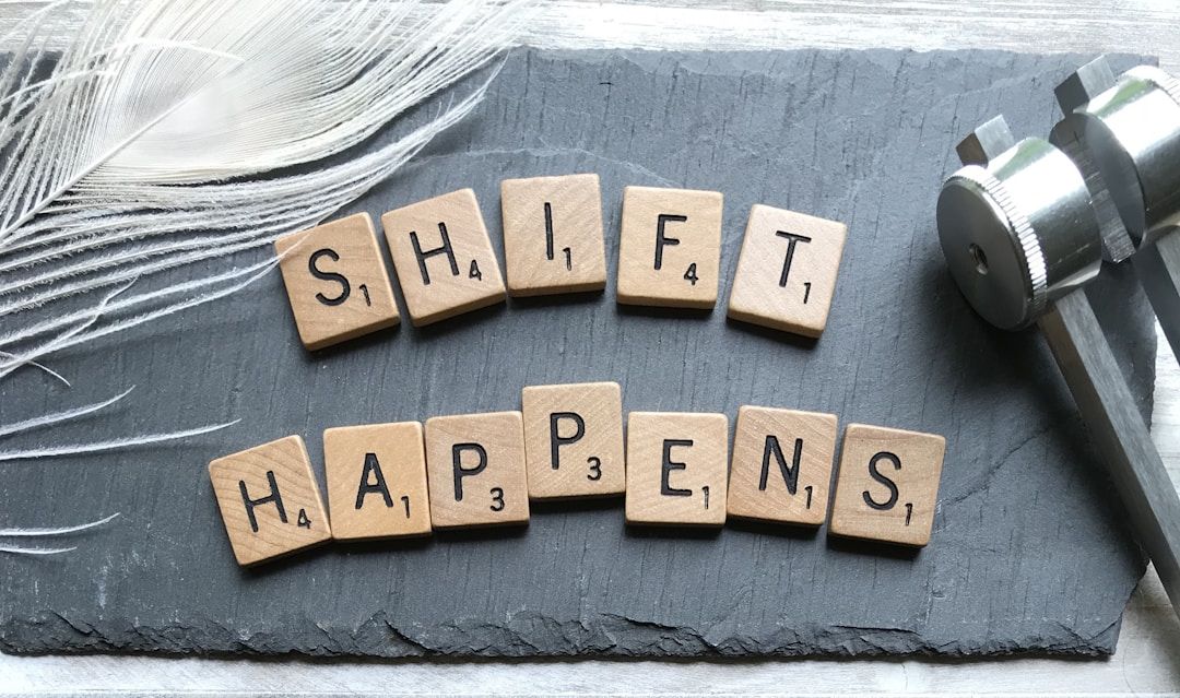 scrabble tiles on a black slate background with a feather and tuning fork that say "shift happens"