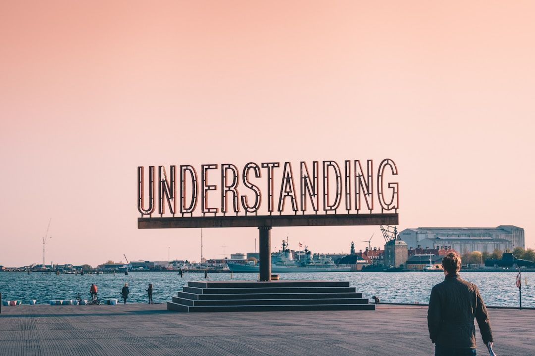 a big sign on the ocean with a pink sunset in the background that says "Understanding" the gift of gene key 4