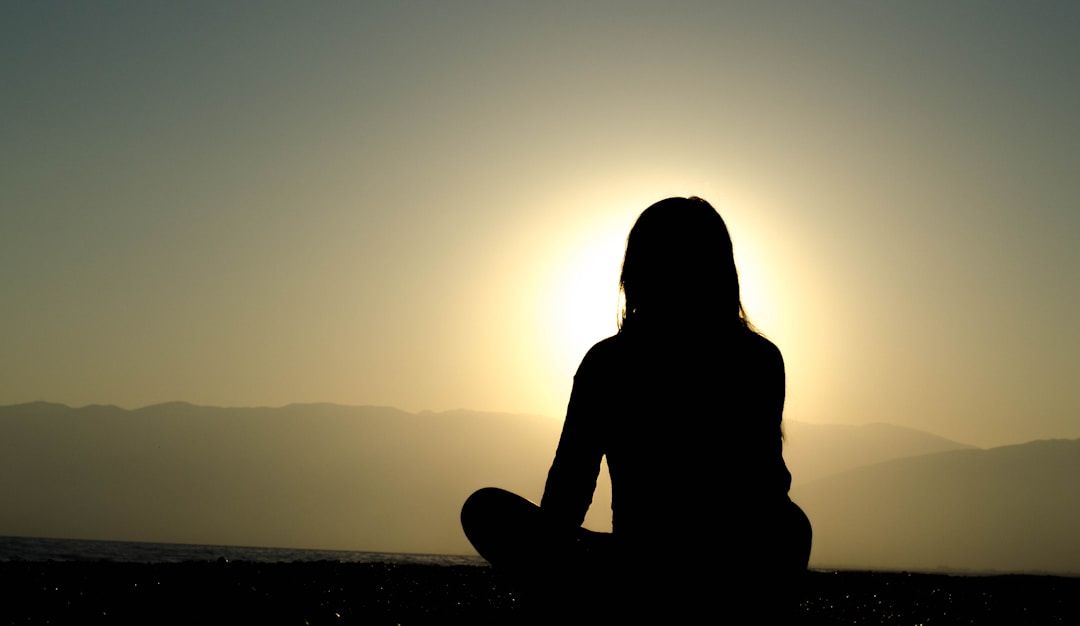 silhouette of a person meditating with mountains in front of them and the sun forming a halo around them