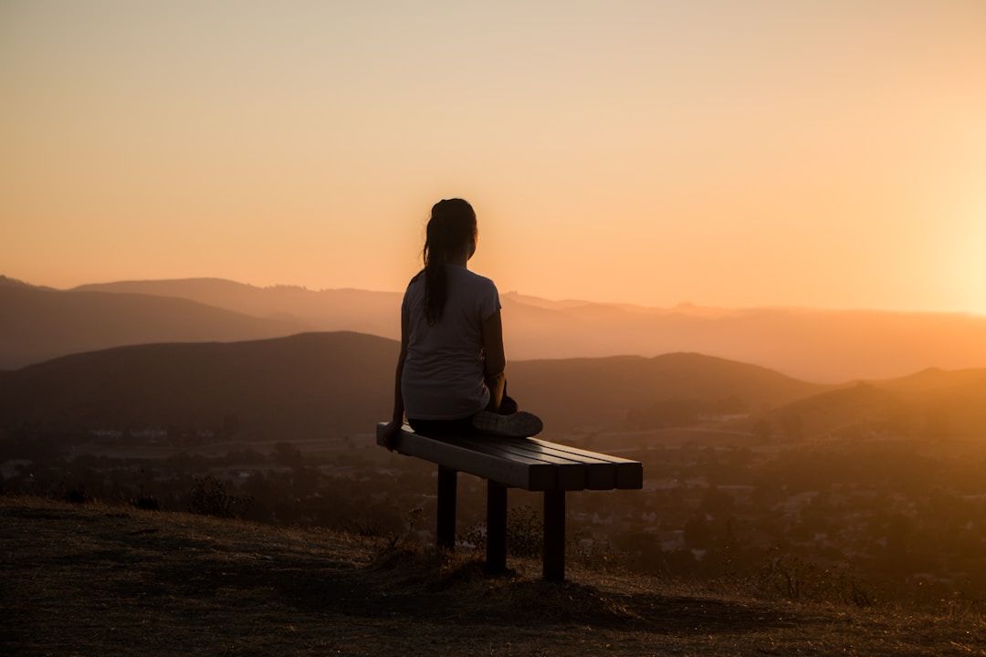 a girl sitting on a bench overlooking the mountains with a peaceful peach toned sunrise