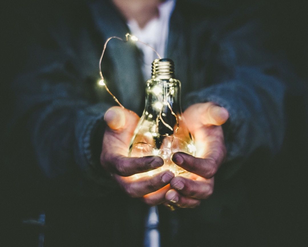 hands holding a clear glass lightbulb filled with a string of fairy lights - a final reminder that gene key 7 is not about control but about surrender to our highest good