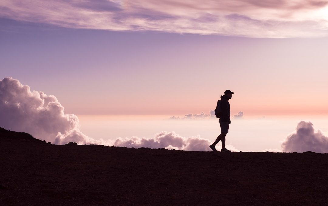 man in silhouette walking on mountain edge with clouds and a pastel sky