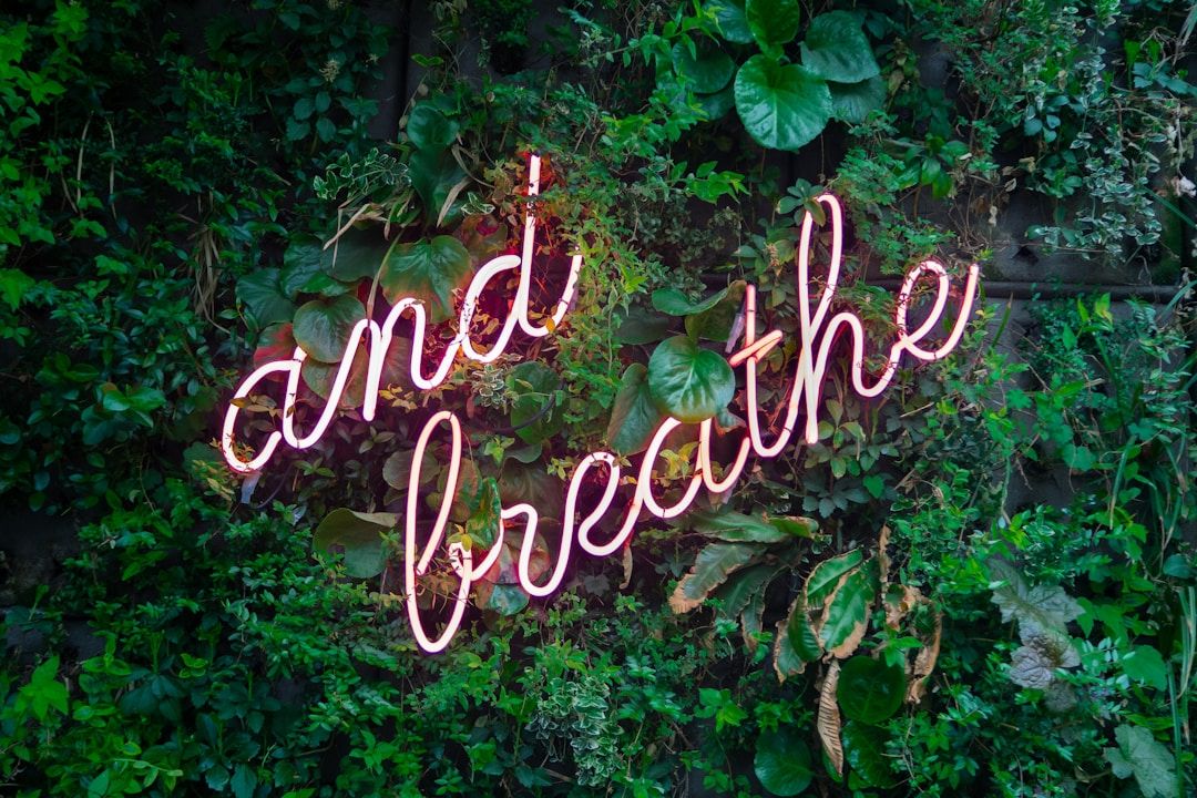 a neon sign that says "and breathe" on a lush green leafy backdrop