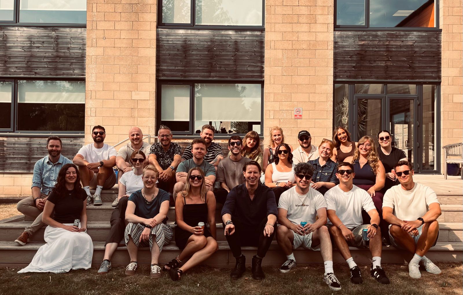 The Showing Up team outdoors on the steps of a stone building on a sunny day, sitting together in two rows.