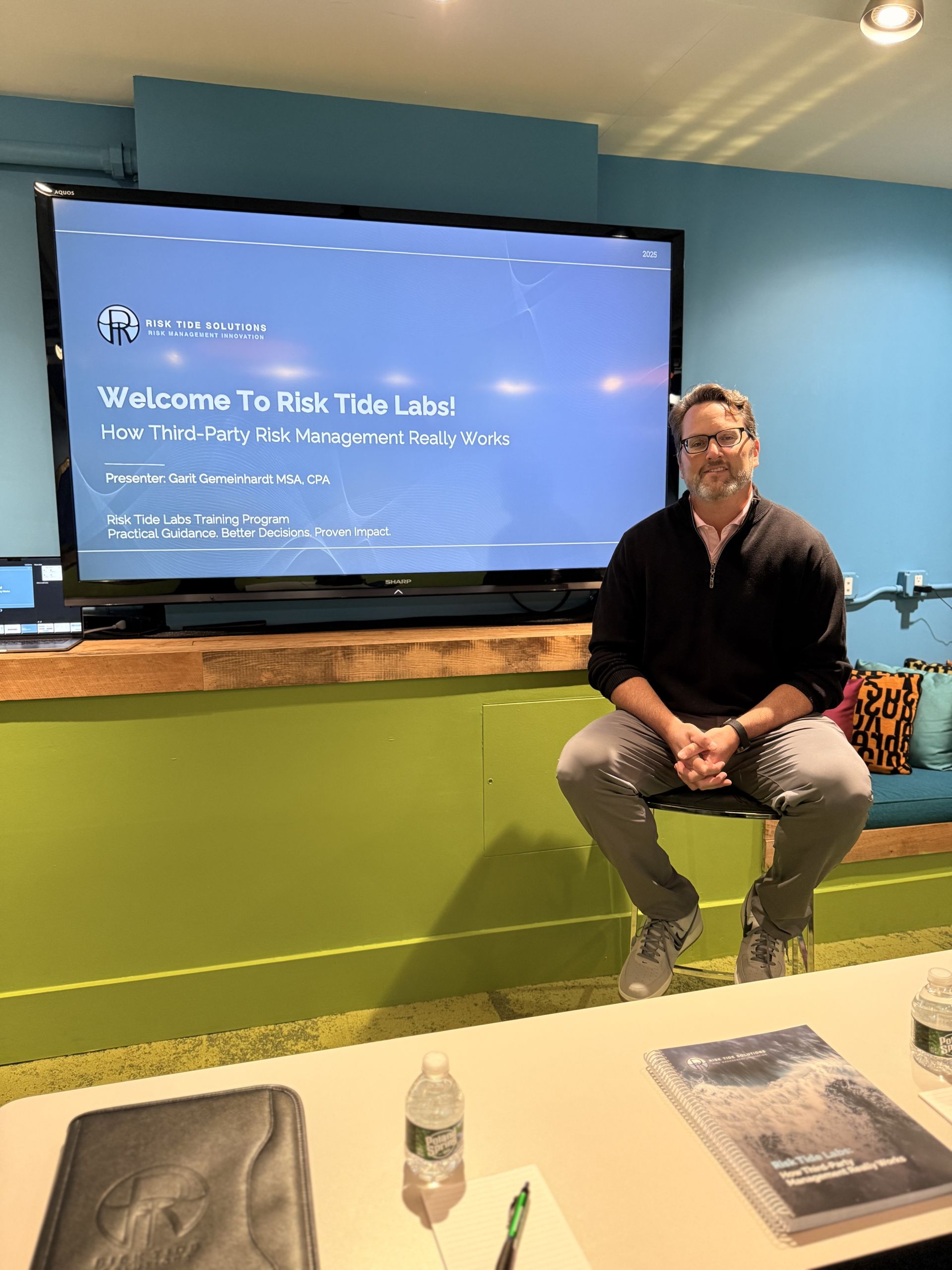 Garit Gemeinhardt hosting a Risk Tide Labs session in front of the welcome slide, with the branded guidebook on the table