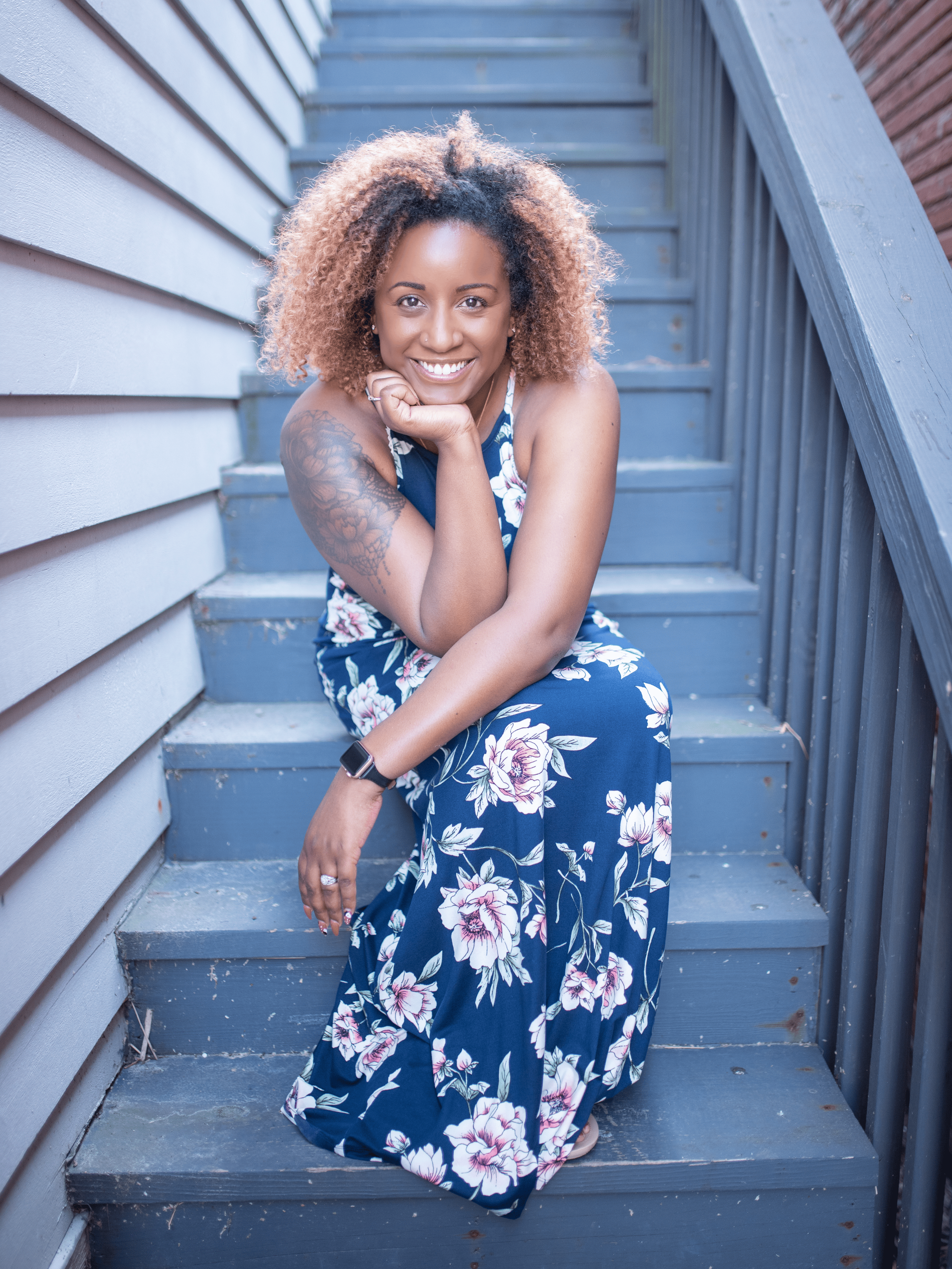 Charla Yearwood, LCSW—Social Work Consultant and Instructor at Doin' The Work LLC, therapist, and founder of Connected in Community—sitting on outdoor stairs, smiling warmly in a floral dress, featured for her commitment to justice-driven mental health care.