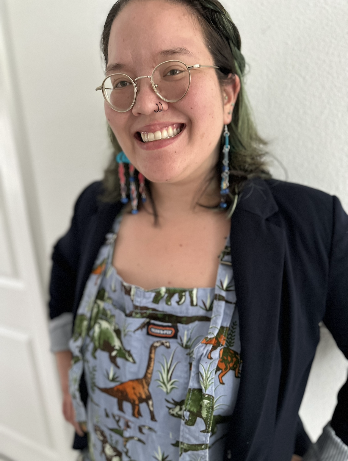 Shimon Cohen, LCSW—Founder and CEO of Doin' The Work LLC, host of the Doin' The Work podcast, therapist, and advocate for justice-based social work—standing in front of greenery wearing a 'Doin' The Work: Frontline Stories of Social Change' t-shirt.