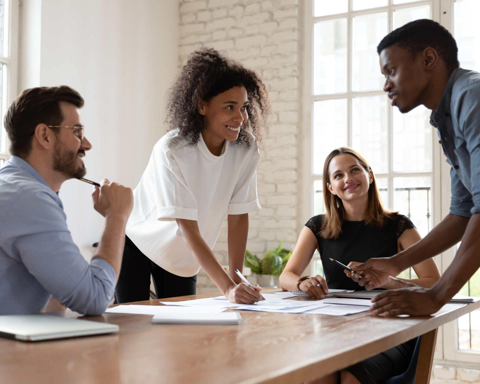 Four diverse professionals engaged in a collaborative meeting around a conference table, smiling and discussing documents, symbolizing inclusive, socially conscious learning and teamwork.