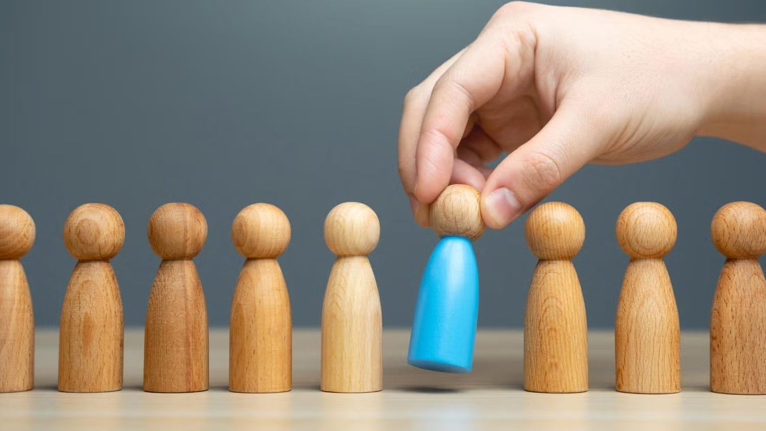 hand lifting blue painted wooden person figurine from line of unpainted ones