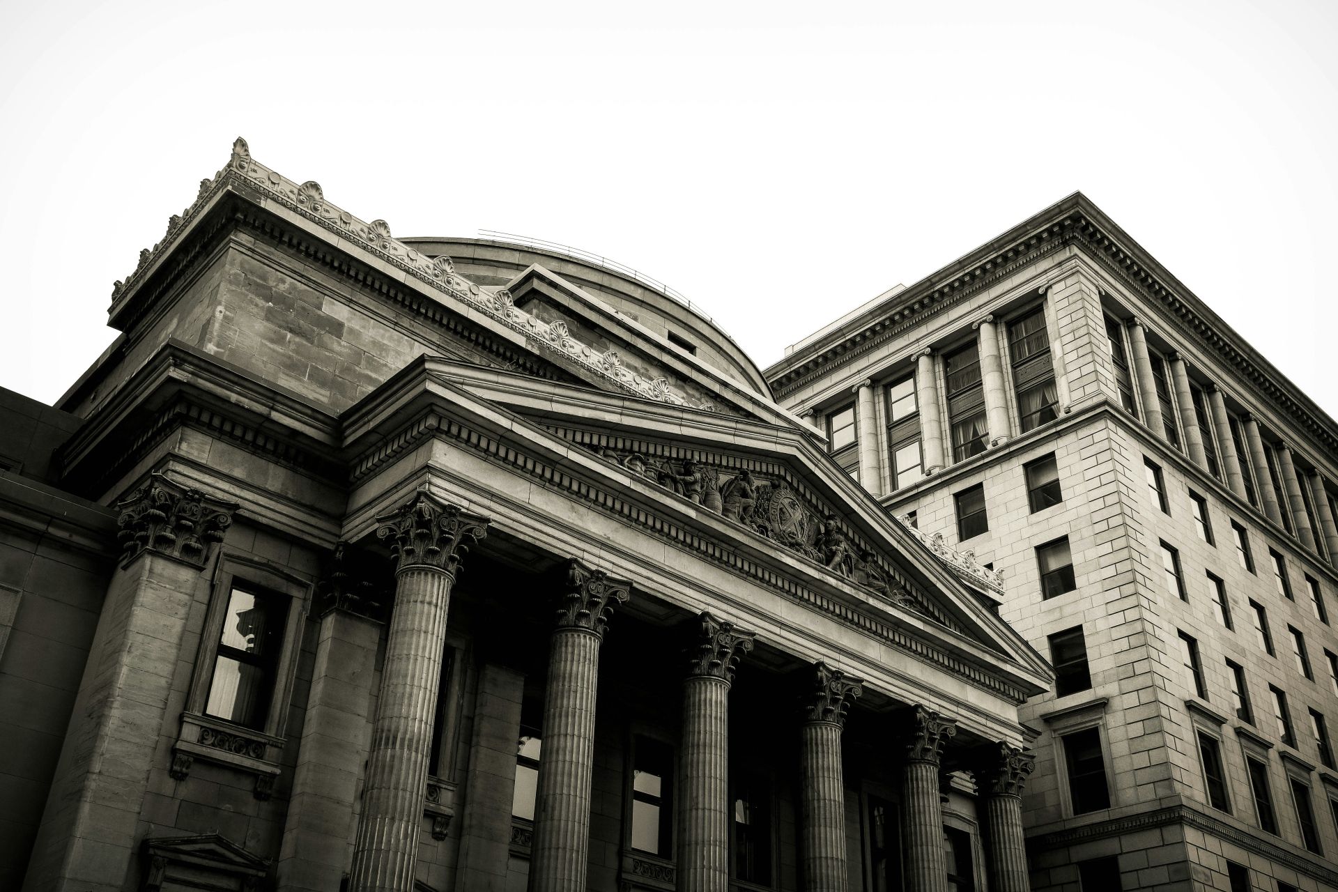a classic, ornate bank building with tall columns and a domed roof in the foreground, set against a slightly taller, simpler rectangular building