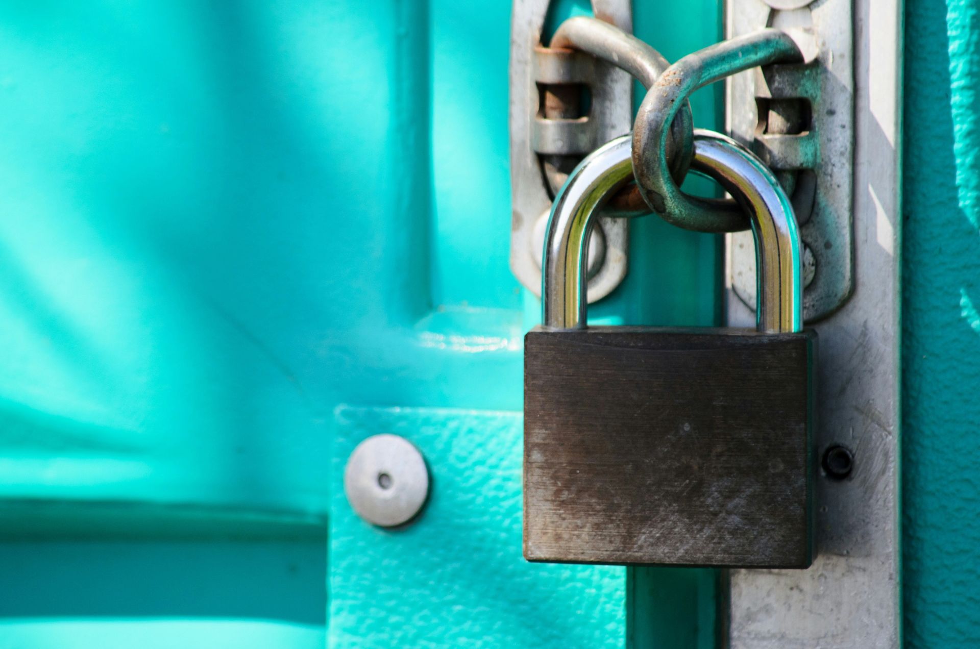 a sturdy silver padlock secures a teal door with a chain