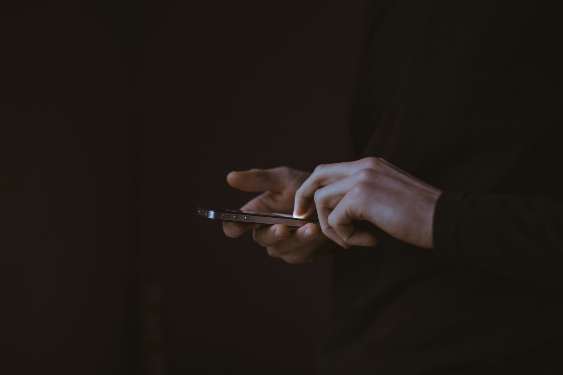 a person in a dark shirt using a smartphone in dim lighting.