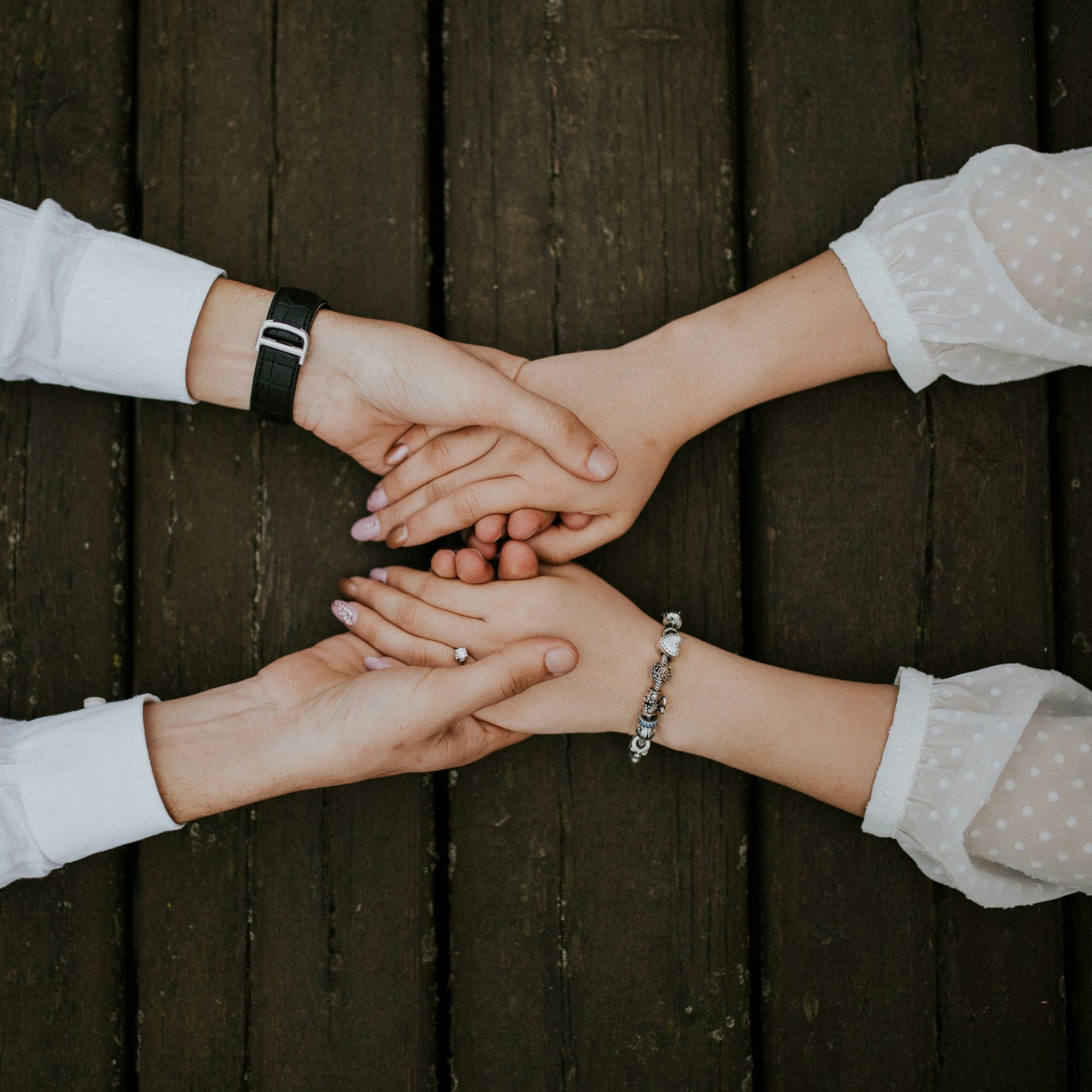 two pairs of hands clasp gently on a wooden surface conveying support or comfort