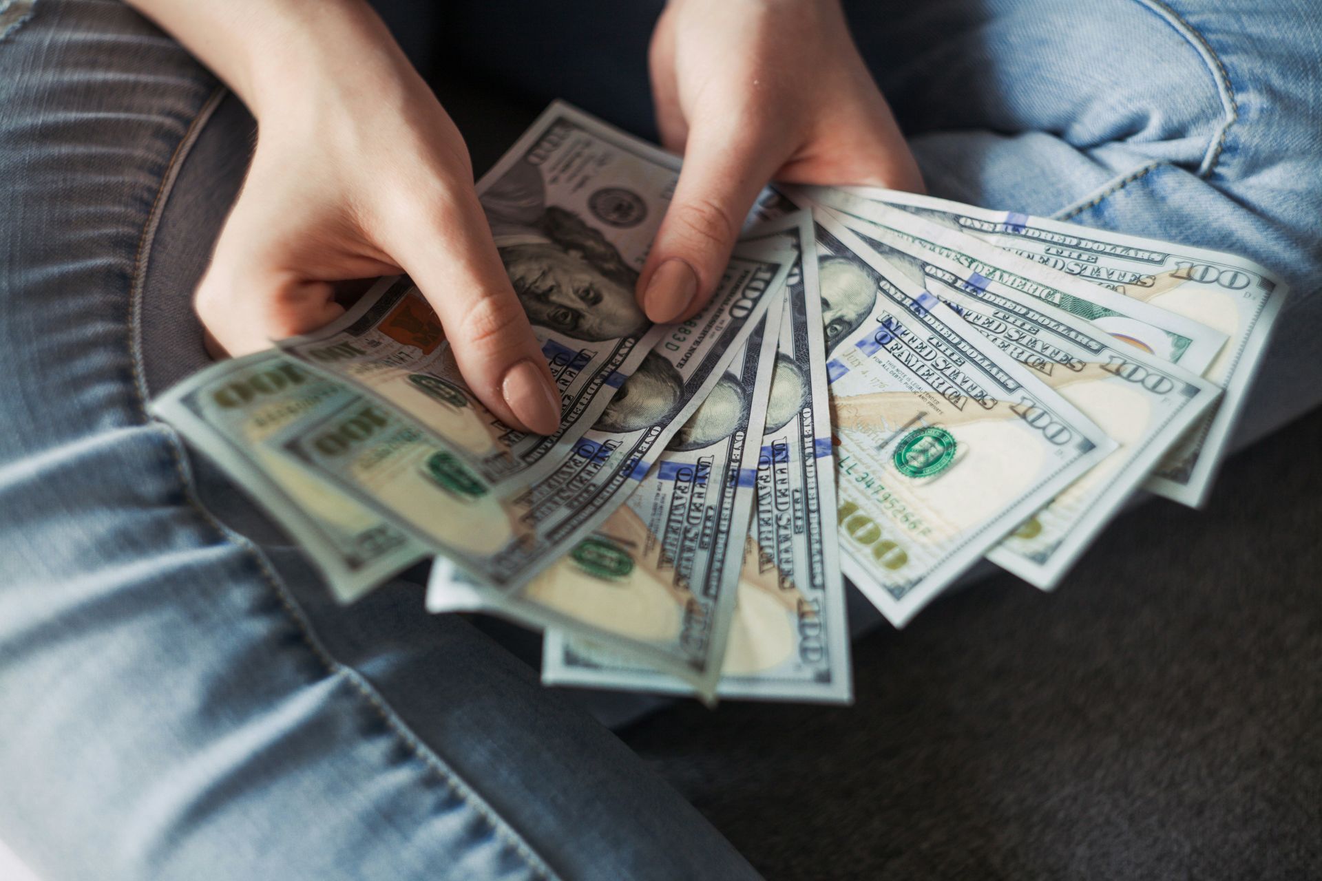 a person in jeans is holding a fan of US hundred-dollar bills