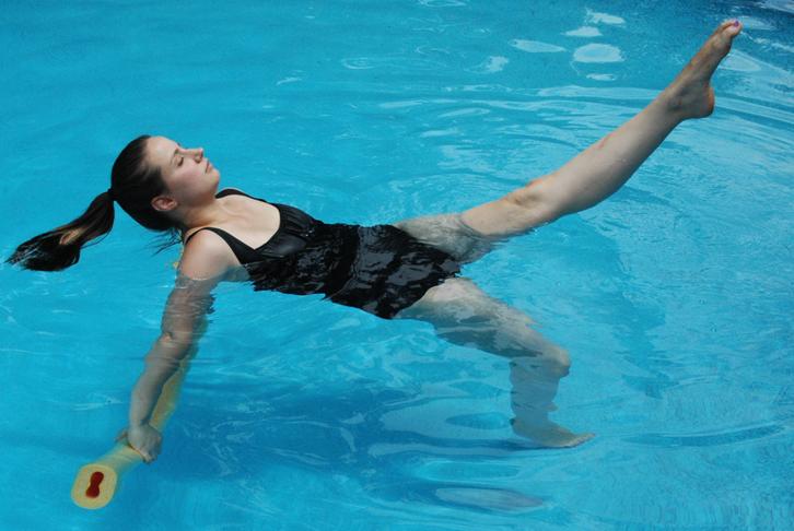A woman performs a high kick in waist-deep water.