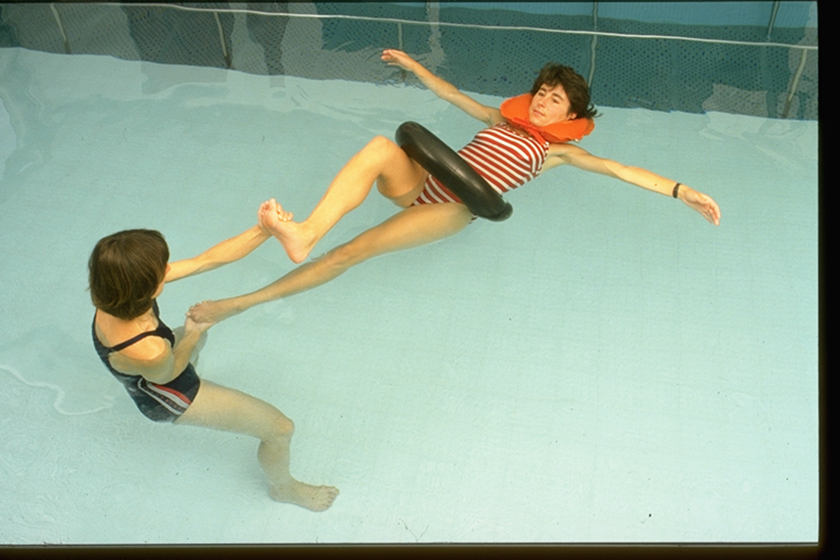 A client floats on rings while a therapist works with her near the pool wall.