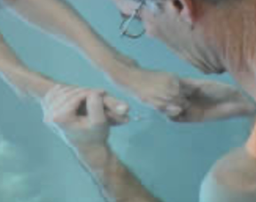 Close-up of a therapist holding a client's hands in the water.