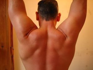 The back and shoulders of a muscular man with his arms raised.