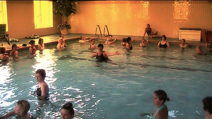 Many people exercise in a large, warmly lit indoor pool.