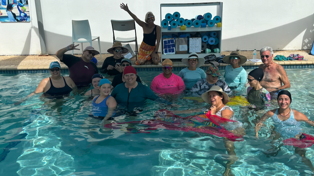 A group of adults gathers in a pool for a group photo.
