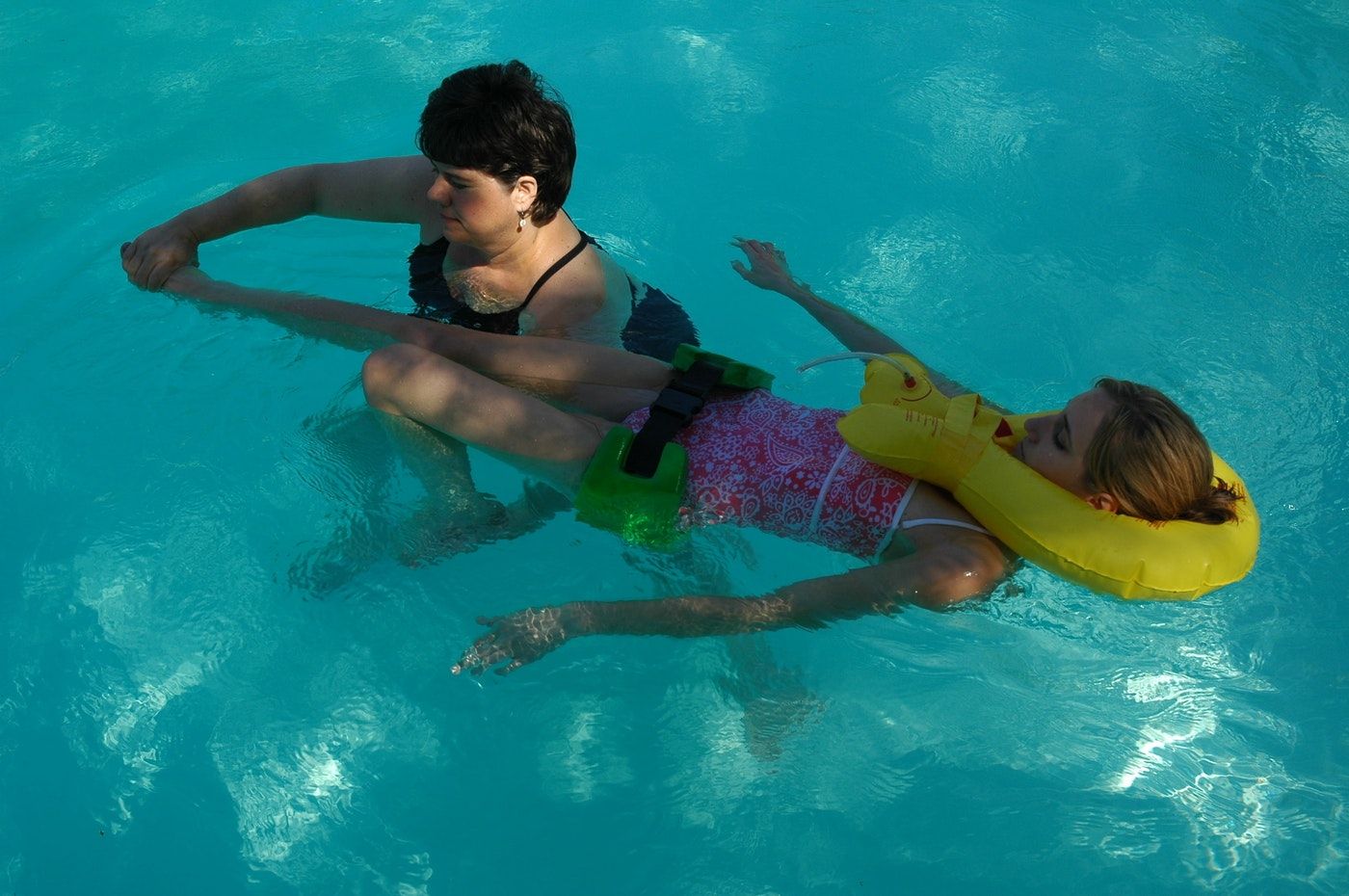 Two swimmers float together, one supported by a yellow float.