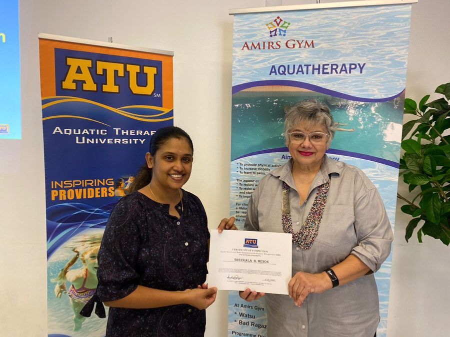 Two smiling women hold an Aquatic Therapy University certificate in front of ATU and Aquatherapy banners